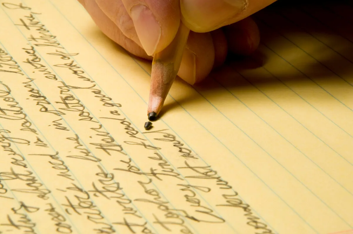 Hand writing dense notes in pencil on yellow lined paper, with the pencil lead broken off at the tip